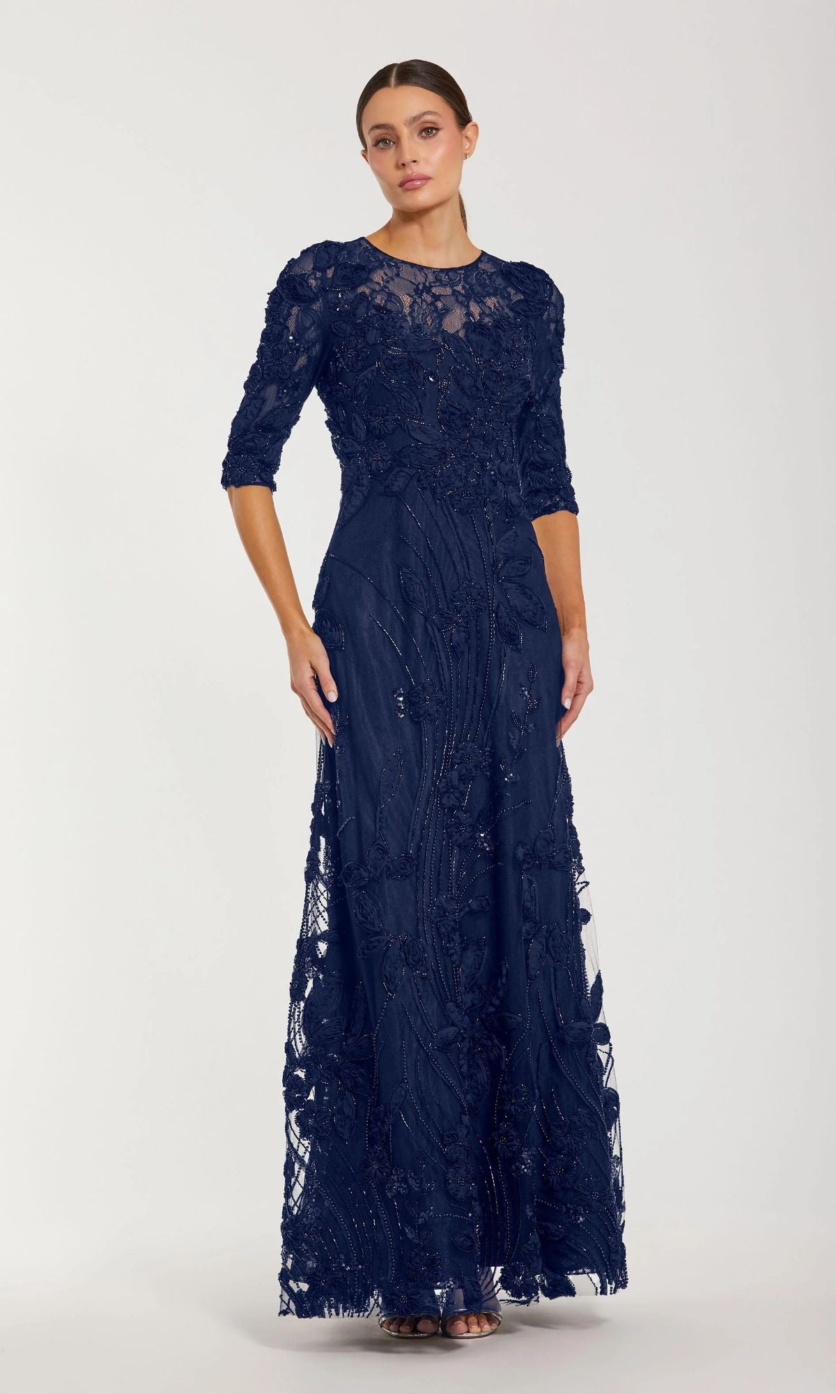 A woman in the Mac Duggal 69016 Long Sleeve Beaded Formal Gown stands against a plain light background—an elegant floor-length navy option, perfect for the mother of the bride.